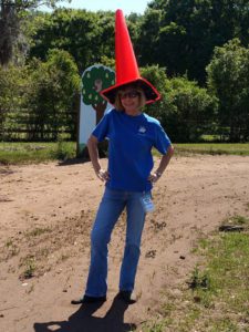 A woman standing in the dirt wearing an orange hat.