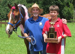 A man and boy holding a trophy next to a horse.