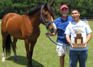 A man and boy holding a trophy next to a horse.