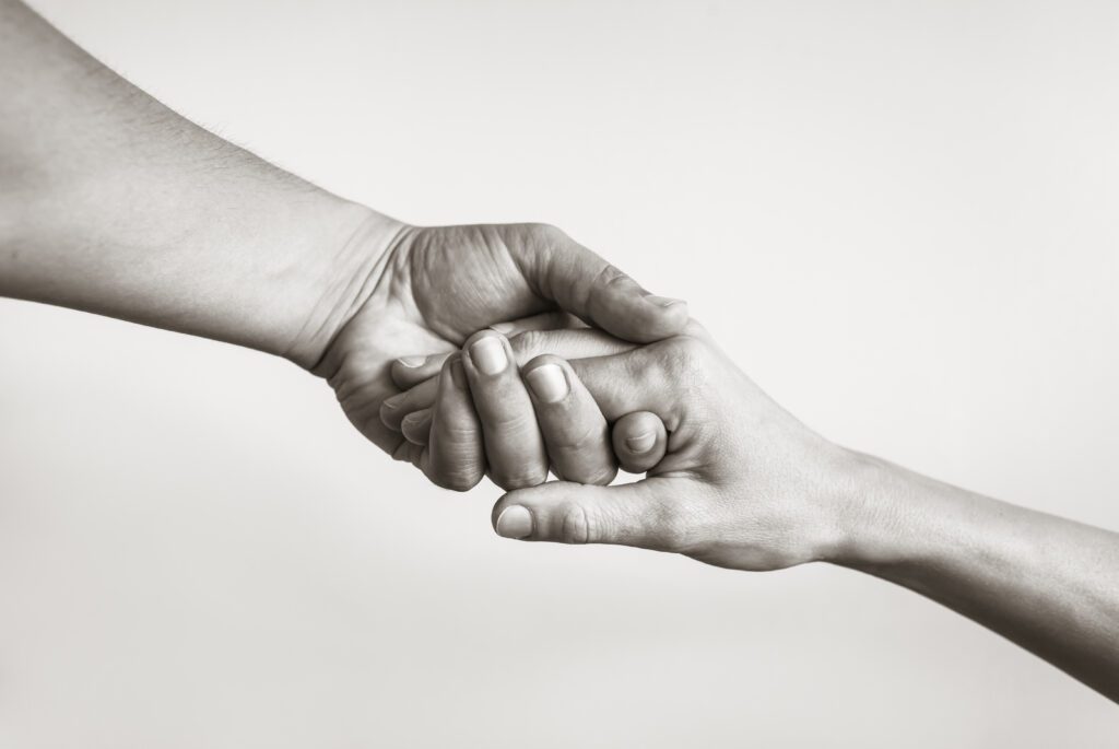 Two hands clasped together in a gentle, supportive manner against a plain background.