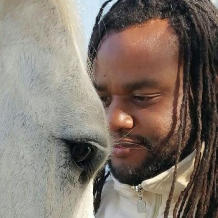 A man with dreadlocks is looking at the nose of a horse.